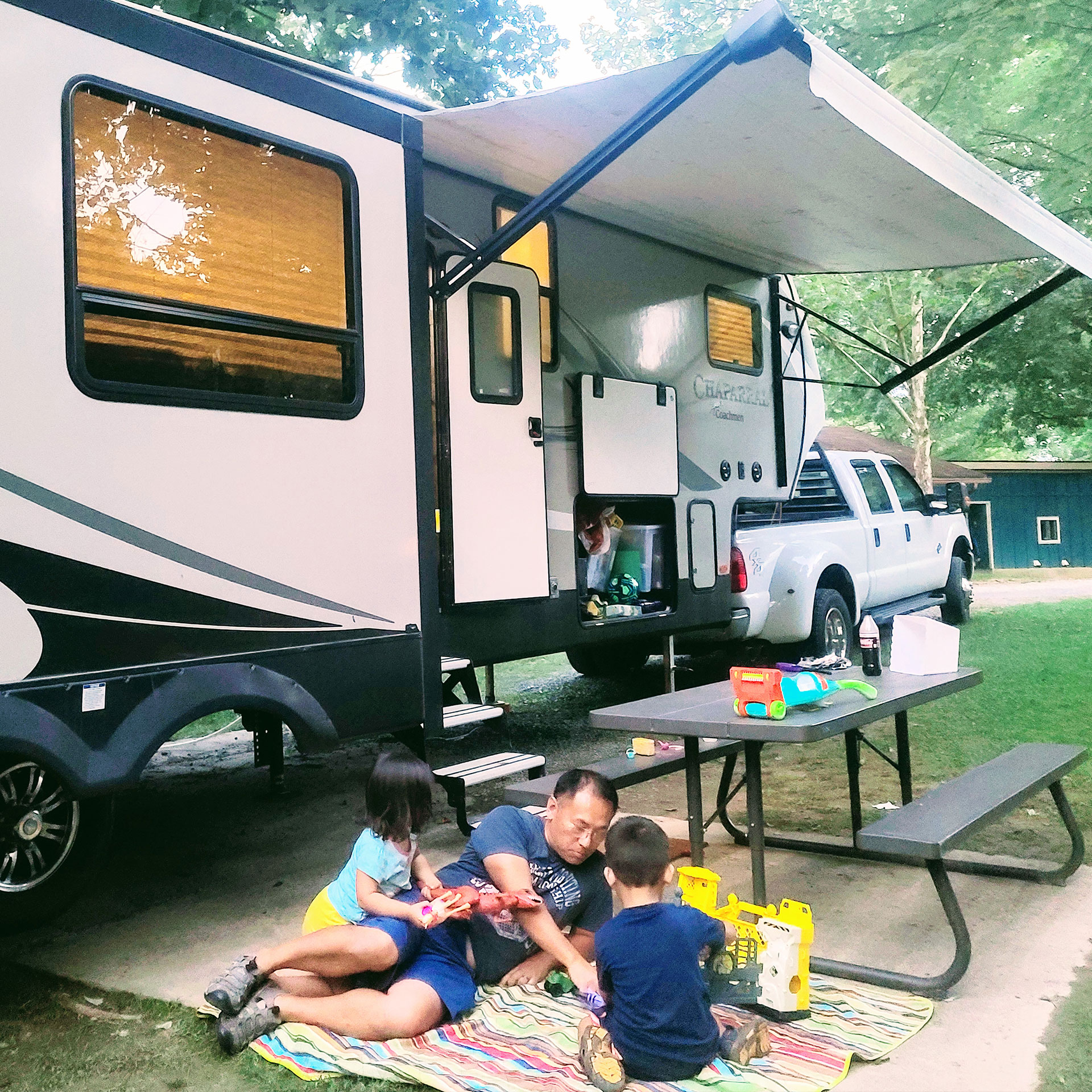 Angelica's husband, Jaques. plays with the children outside of their RV next to a picnic table.
