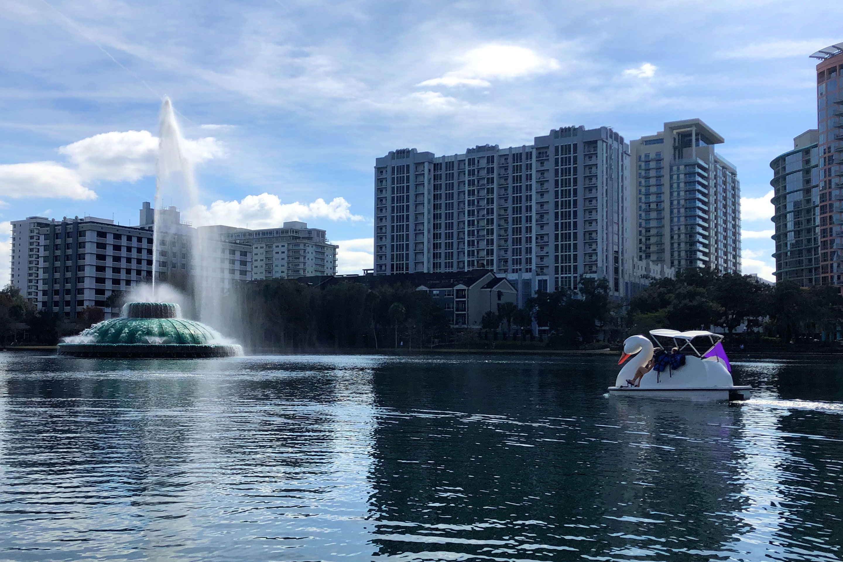 A woman paddles a white Swan boat in Lake Eola under a blue sky.
