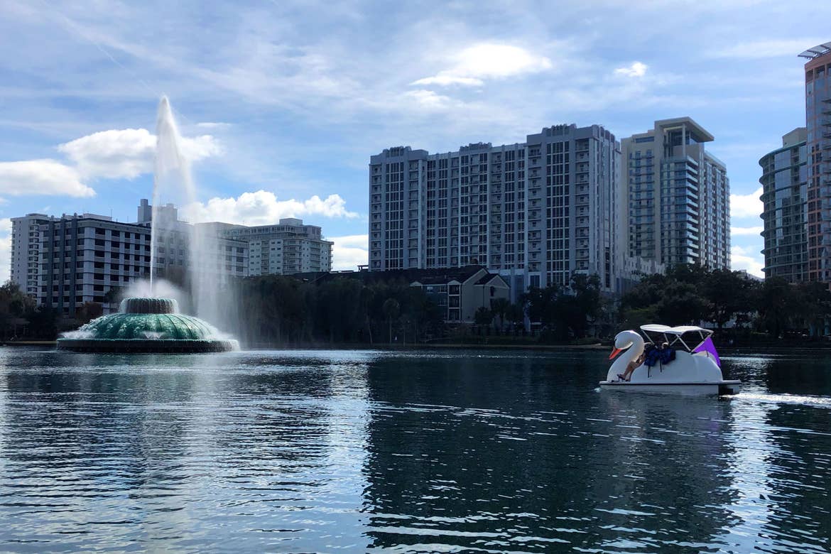 A woman paddles a white Swan boat in Lake Eola under a blue sky.