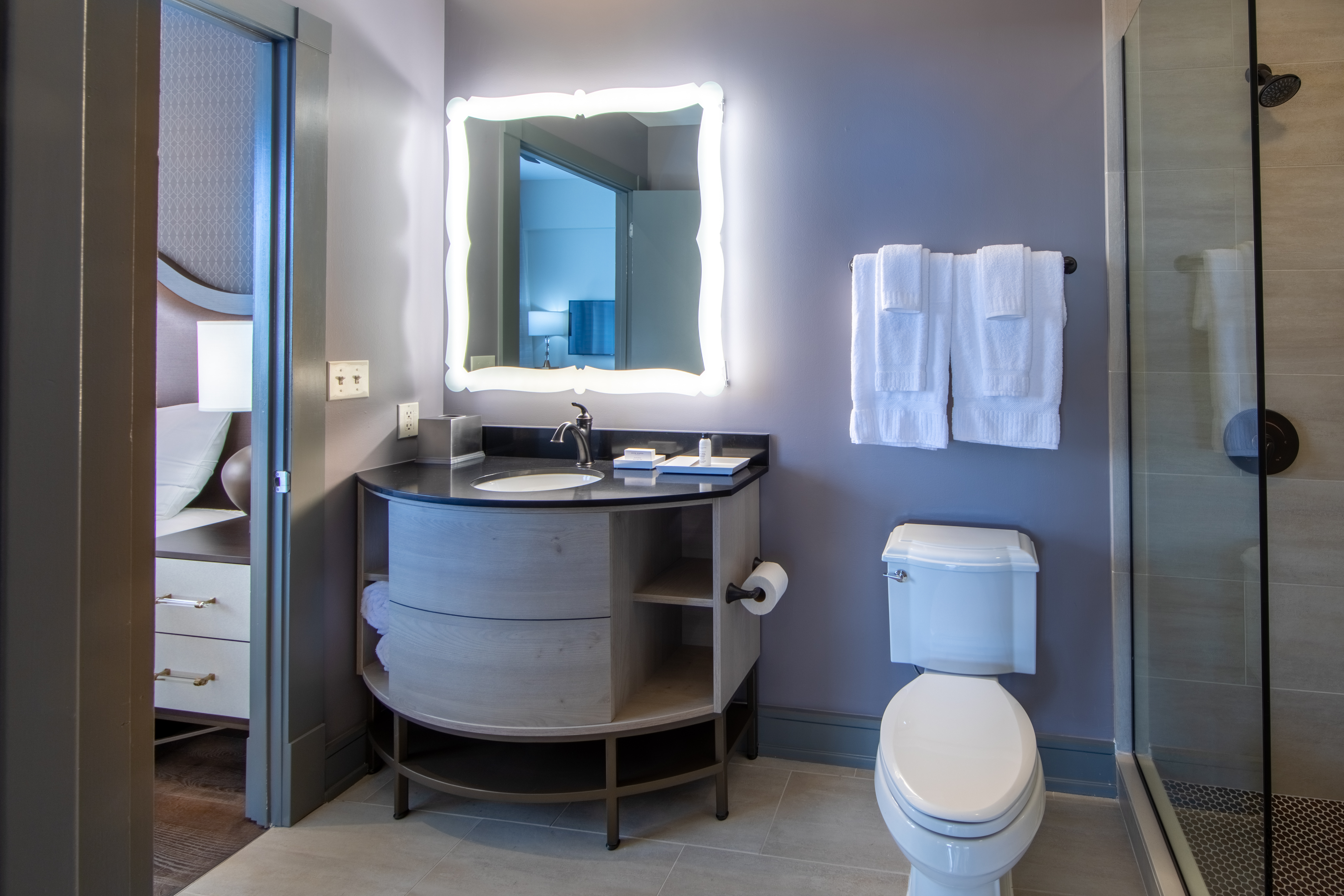 Bathroom attached to bedroom with toilet, walk-in shower and sink with lighted mirror at New Orleans Resort in Louisiana.