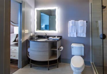 Bathroom attached to bedroom with toilet, walk-in shower and sink with lighted mirror at New Orleans Resort in Louisiana.