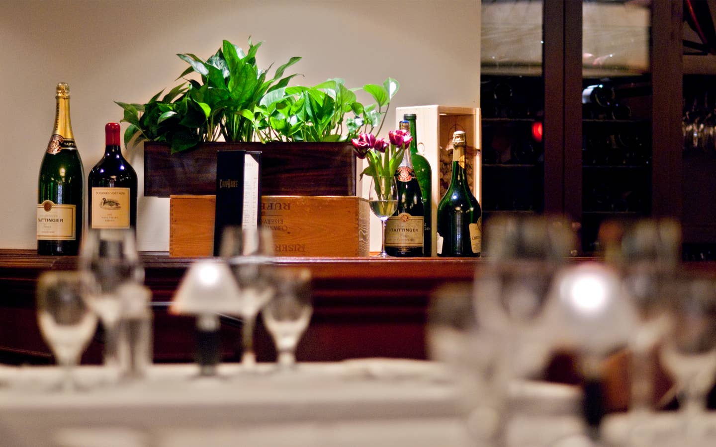 Restaurant table with wine glasses and bottles of wine in the background.