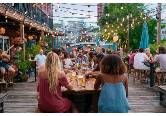 Diners enjoying an outdoor meal on a lively patio decorated with hanging lights and plants.
