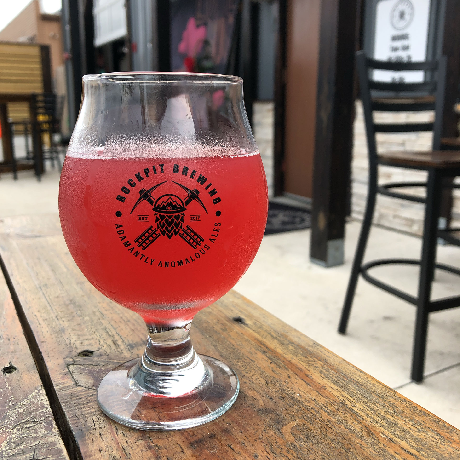 Stemmed beer glass with the 'Rockpit Brewing' logo placed on a wooden plank table outdoors.
