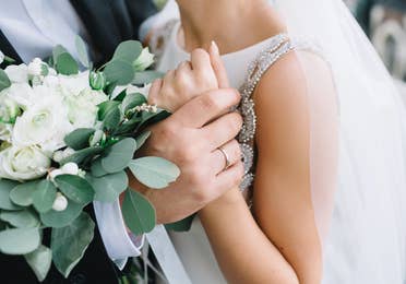 Closeup of bride and groom with wedding flowers and rings.