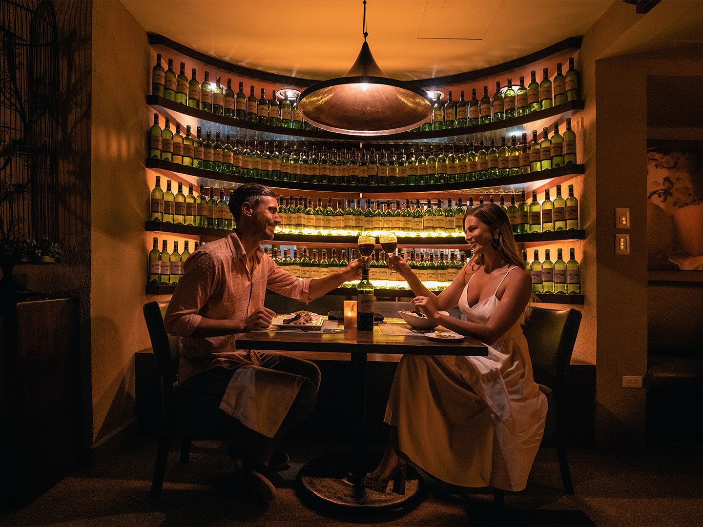 A couple clinking wine glasses surrounded by wine bottles in a restaurant at The Royal Cancun in Cancun, Mexico.