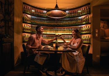 A couple clinking wine glasses surrounded by wine bottles in a restaurant at The Royal Cancun in Cancun, Mexico.