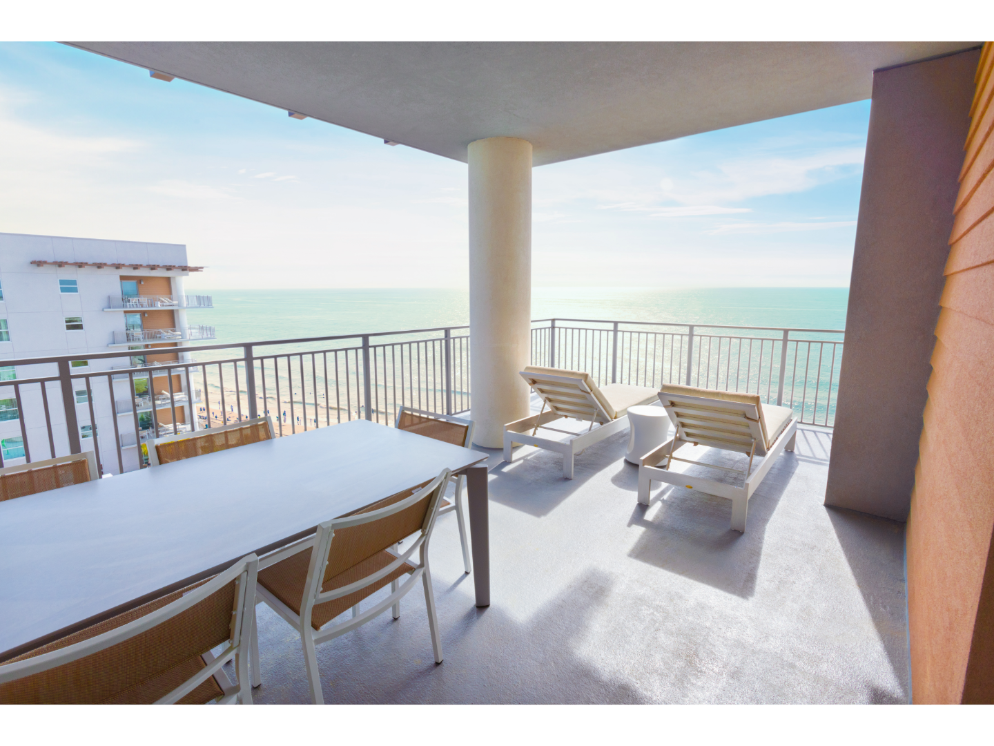 Oceanfront balcony with lounge chairs, dining table, and scenic sea view.