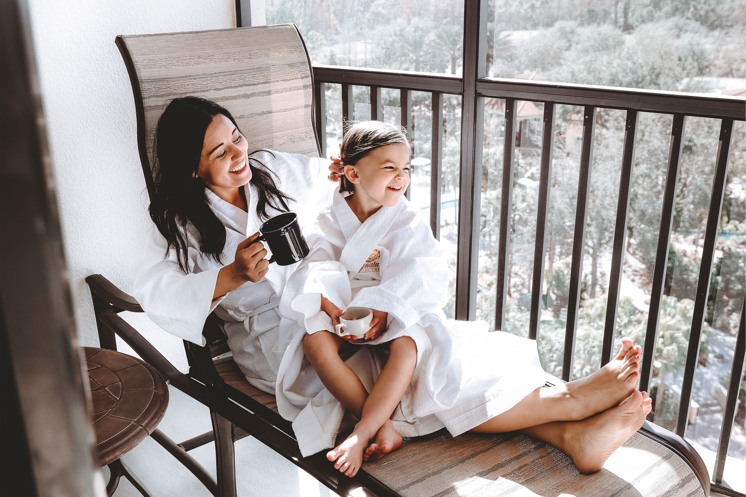 Featured contributor, Mia St. Clair (left), and daughter, Roux (right), enjoy time together wearing white robes and sipping tea on the patio at Orange Lake Resort in Orlando, FL.
