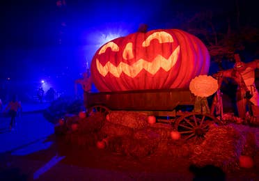 An oversized Jack O' Lantern sits on bales of hay at night.