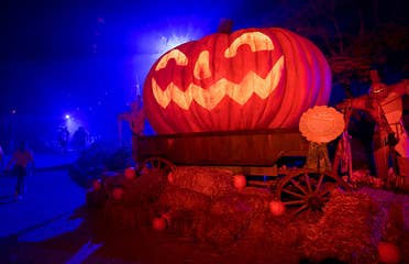 An oversized Jack O' Lantern sits on bales of hay at night.