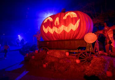 An oversized Jack O' Lantern sits on bales of hay at night.