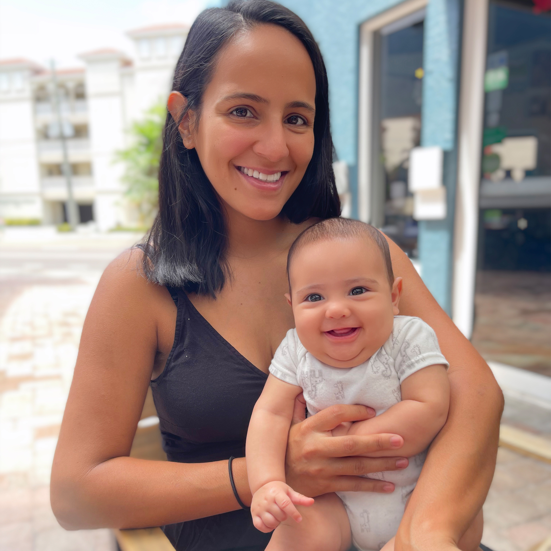 A woman holds a newborn baby boy at an outdoor dining table.
