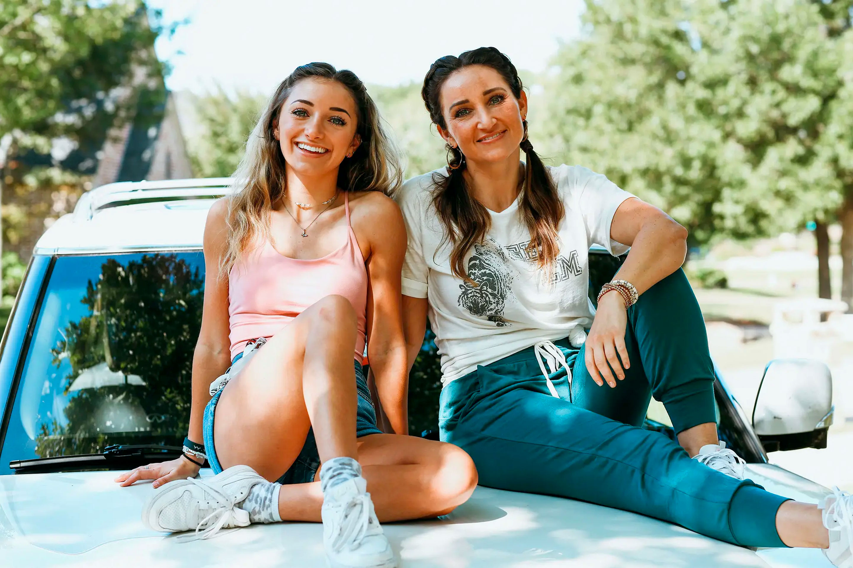 Mindy McKnight (right) and daughter (left) sit outdoors on the hood of a white SUV.