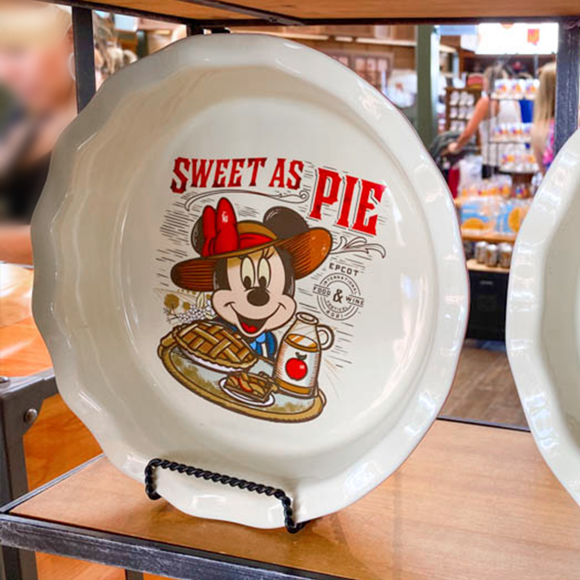 A ceramic pie dish featuring Minnie Mouse in a sunhat reads, 'Sweet as Pie' as it stands propped on a shelf.