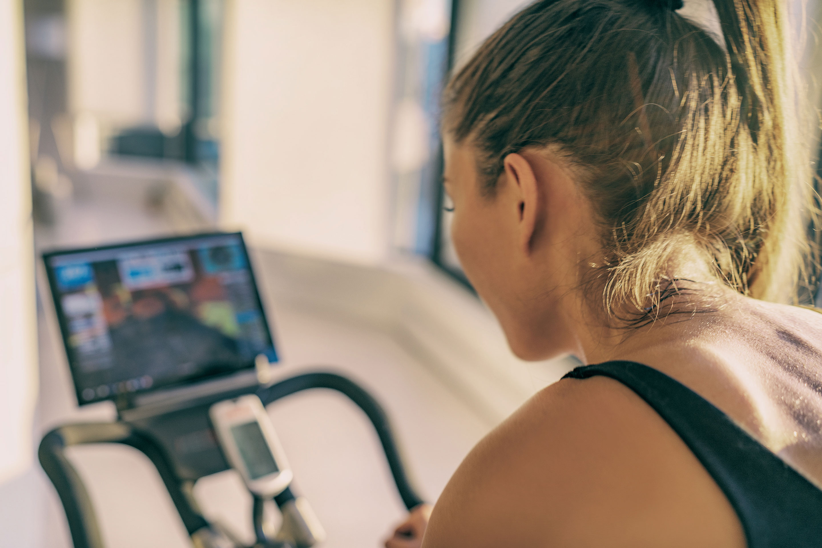 A woman rides an exercise bike while watching a virtual cycle class.
