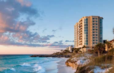 Clouds glowing pink float over rocky shoreline at sunset.