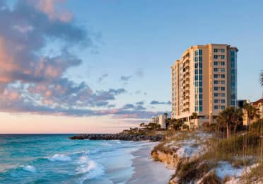 Clouds glowing pink float over rocky shoreline at sunset.