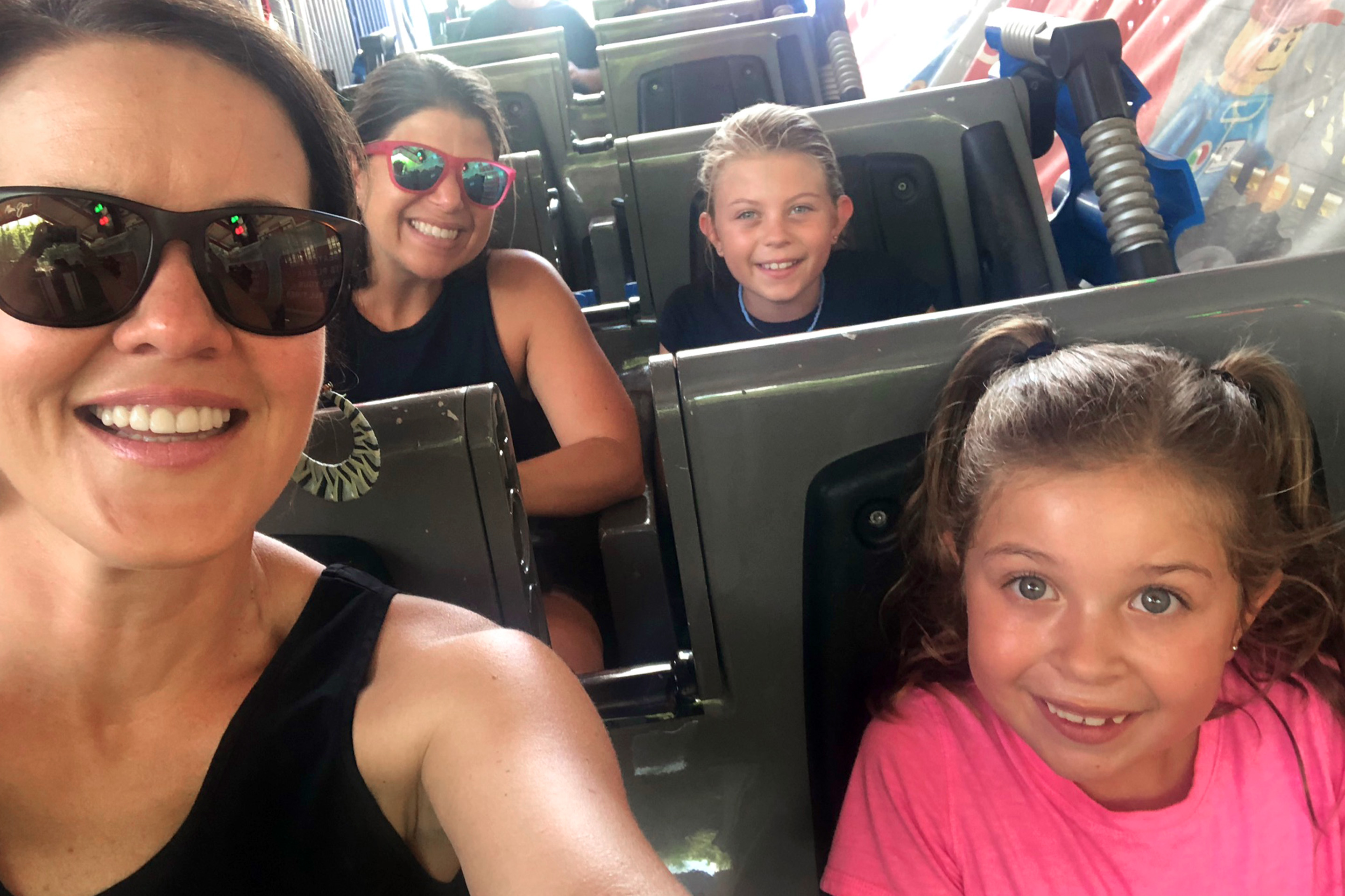 Two women (left) and two young girls (right) are seated on a roller coaster vehicle.