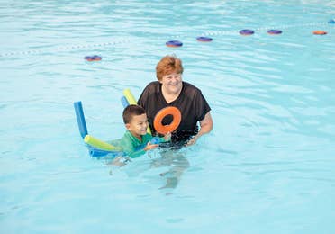 Woman helping child float on pool tubes in outdoor pool at Holiday Hills Resort in Branson, Missouri.