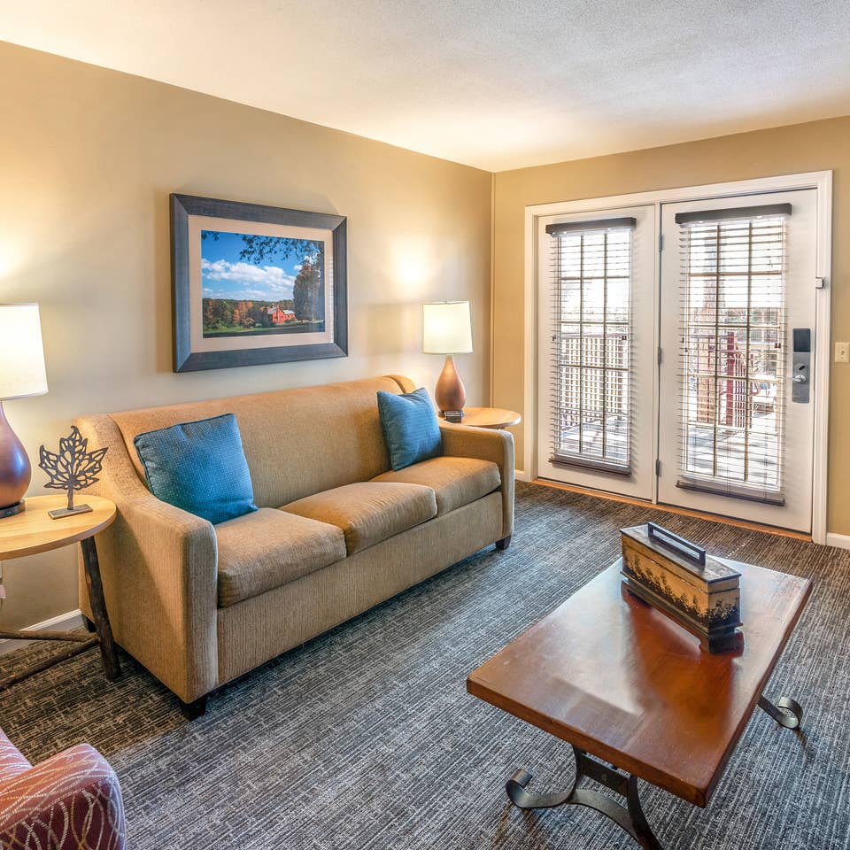 Living room with a sofa, two chairs, and tables in a one bedroom villa at Oak n' Spruce Resort in South Lee, Massachusetts