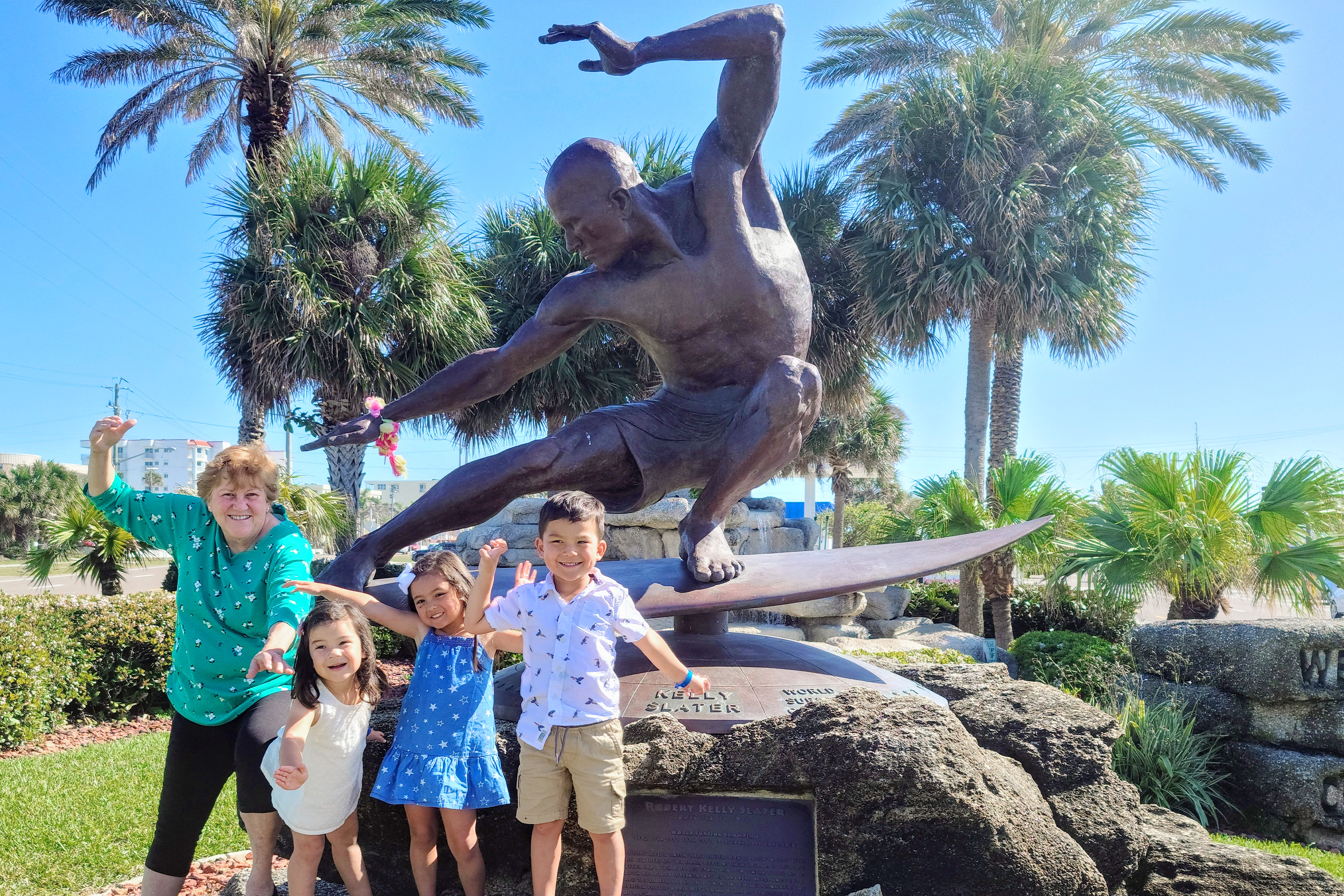 Featured Contributor, Angelica Kajiwara's mother and three children pose in front of a statue of Kelly Slater in downtown Cocoa Beach.