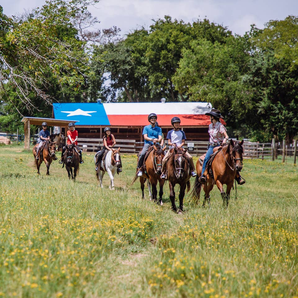 Group of guests riding horses through a field at Villages Resort in Flint, Texas.