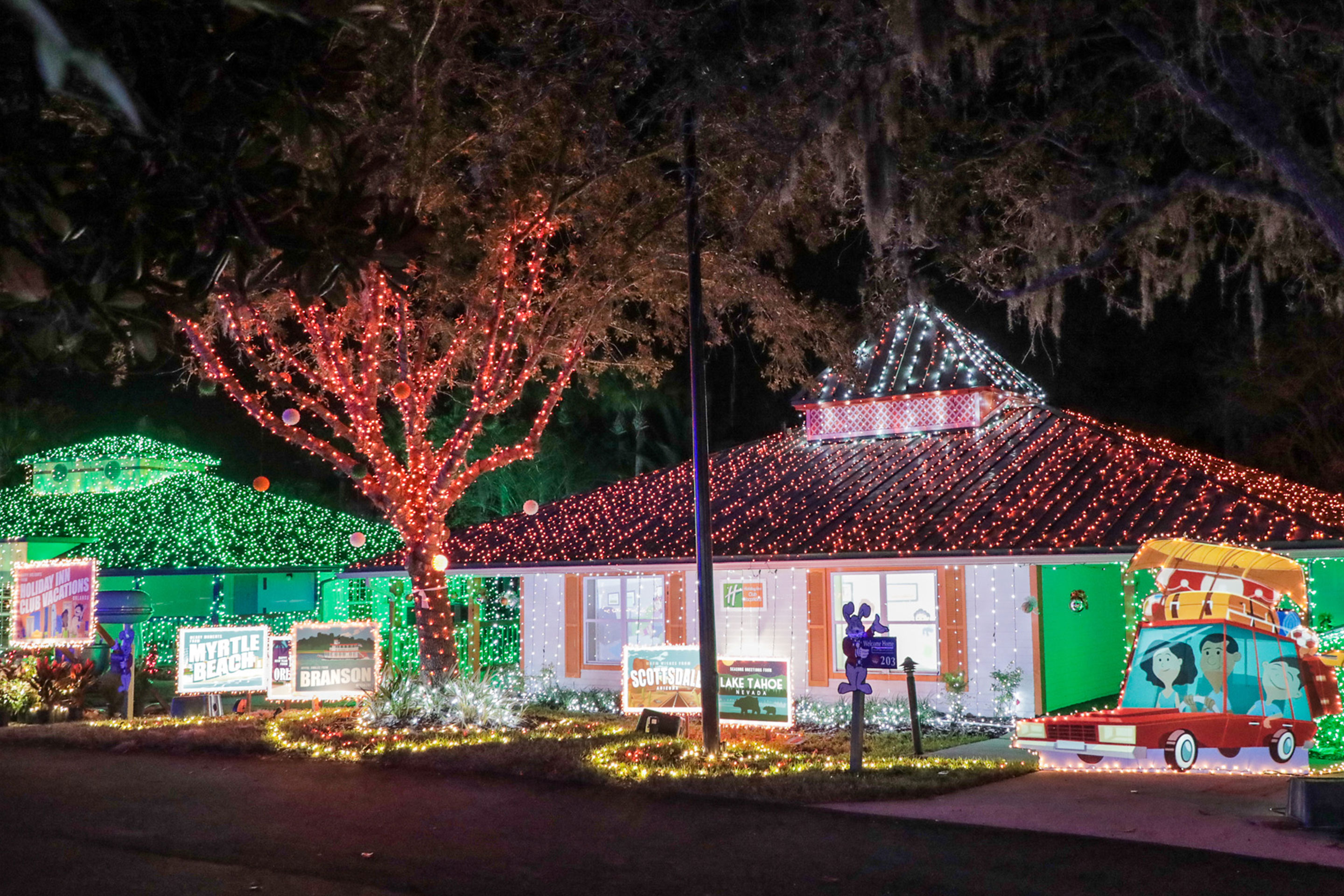 A nighttime exterior of the HICV Villa with colorful string lights and giant postcard decorations.