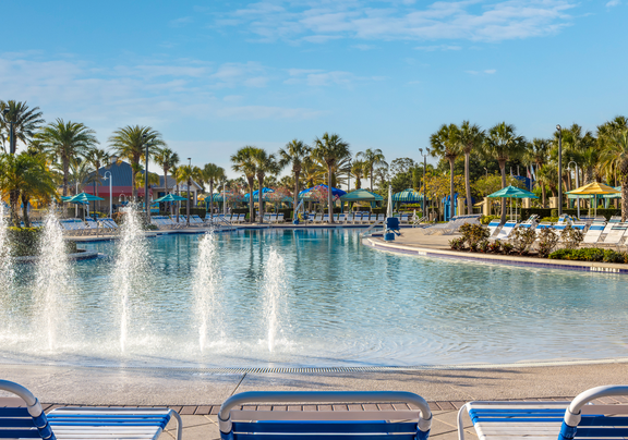 Resort pool with blue loungers and palm trees under a clear sky.