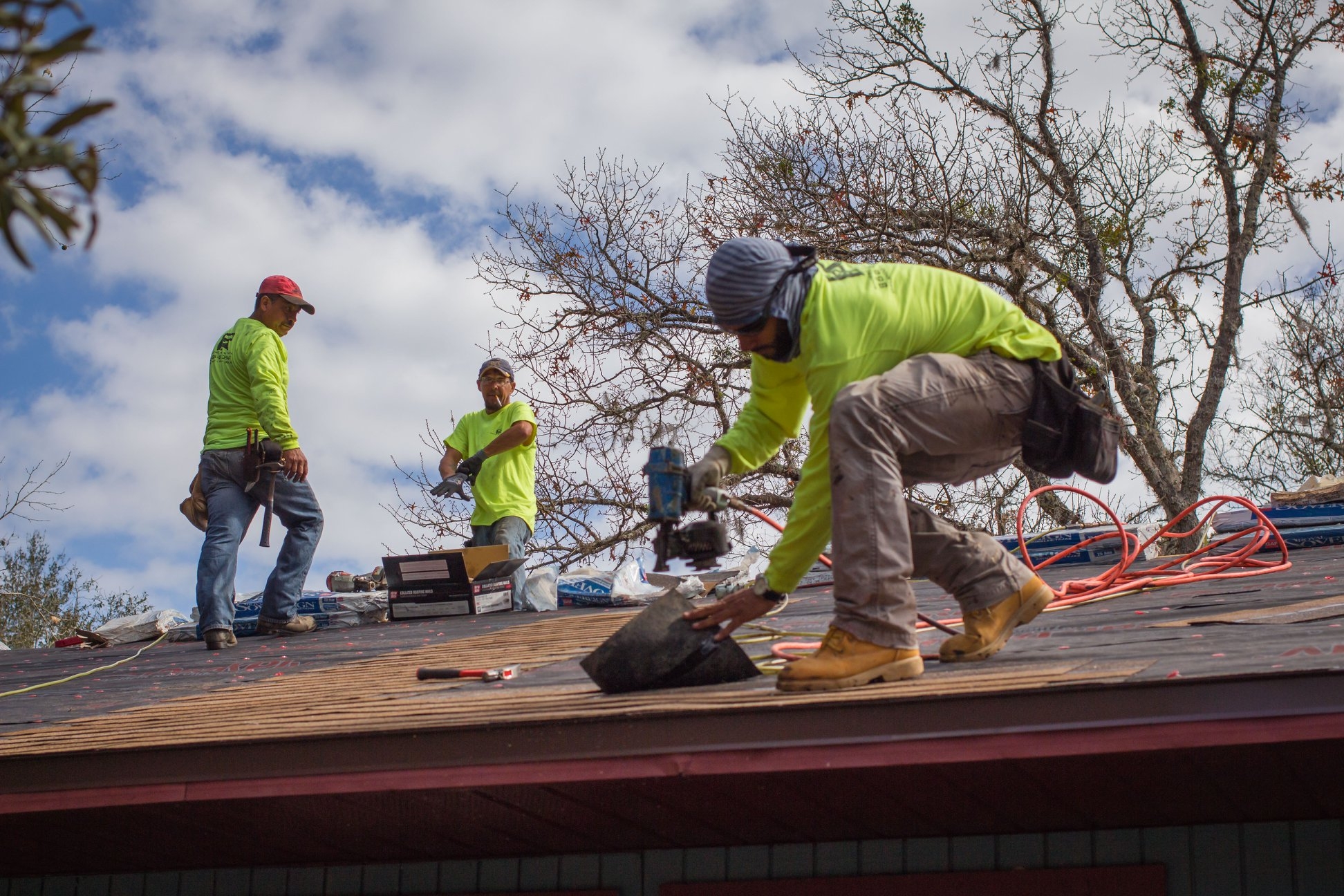 Three men nailing new shingles onto a roof