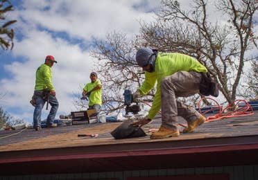 Three men nailing new shingles onto a roof