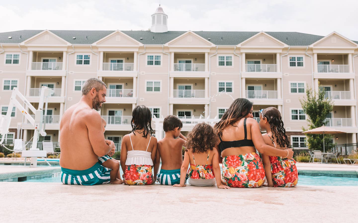 Mother, father, and five children sitting at the edge of a pool at Holiday Inn Club Vacations Williamsburg Resort in Virginia.