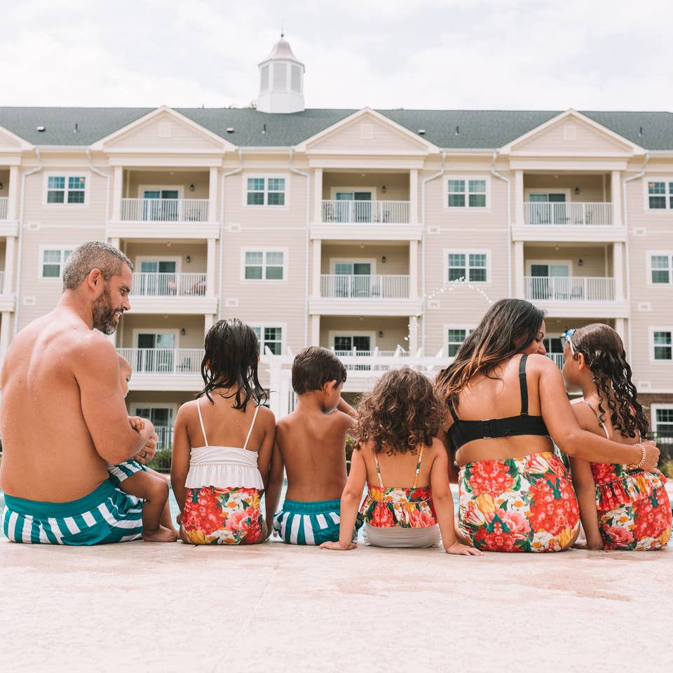 Mother, father, and five children sitting at the edge of a pool at Holiday Inn Club Vacations Williamsburg Resort in Virginia.