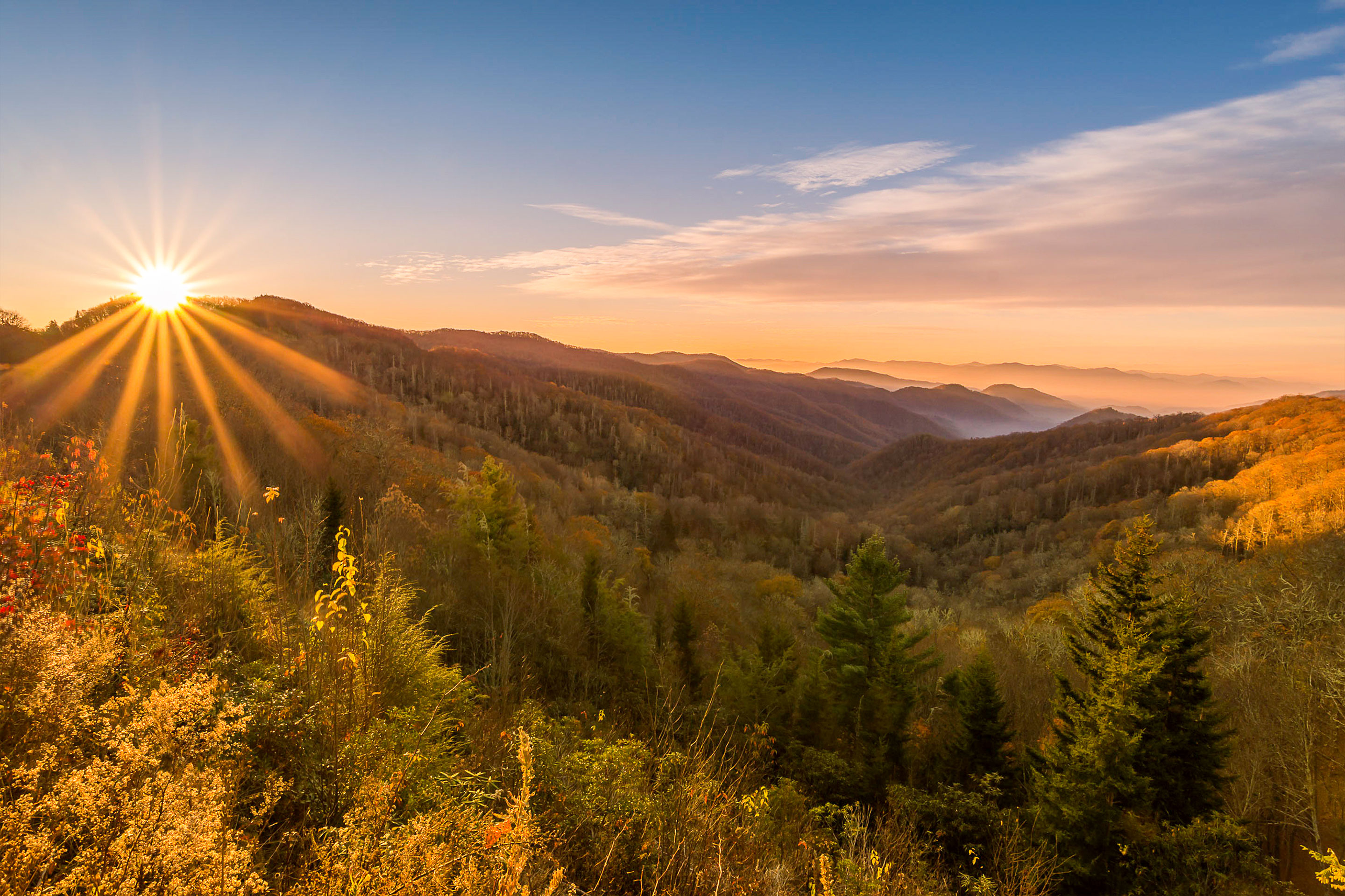 A sun sets at the peak of a mountain range in the fall.