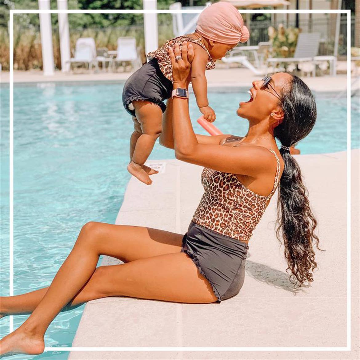 A woman holding her baby in the air next to the pool