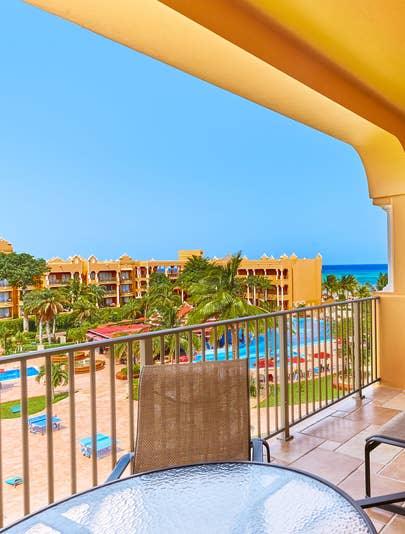 View from a balcony, across from a portion of a suite building, overlooking the garden pool surrounded by blue beach chairs, palm trees and a tease of the ocean, at The Royal Haciendas, at Playa del Carmen, Mexico