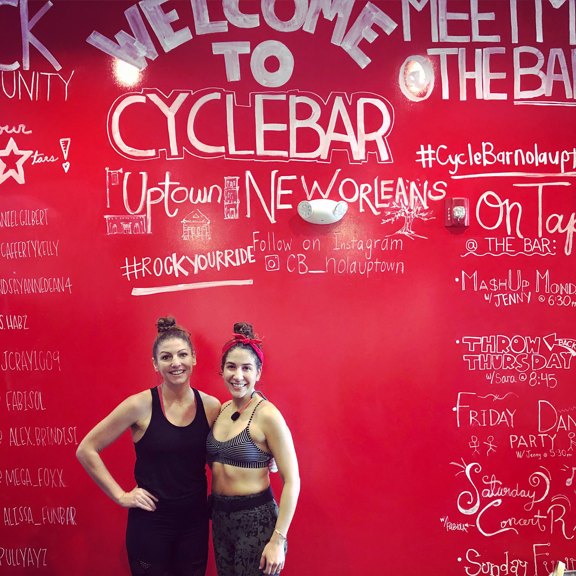 Co-author, Christine (left), wears a black tank top and shorts while posing with a fellow cycle bar instructor at New Orleans location.