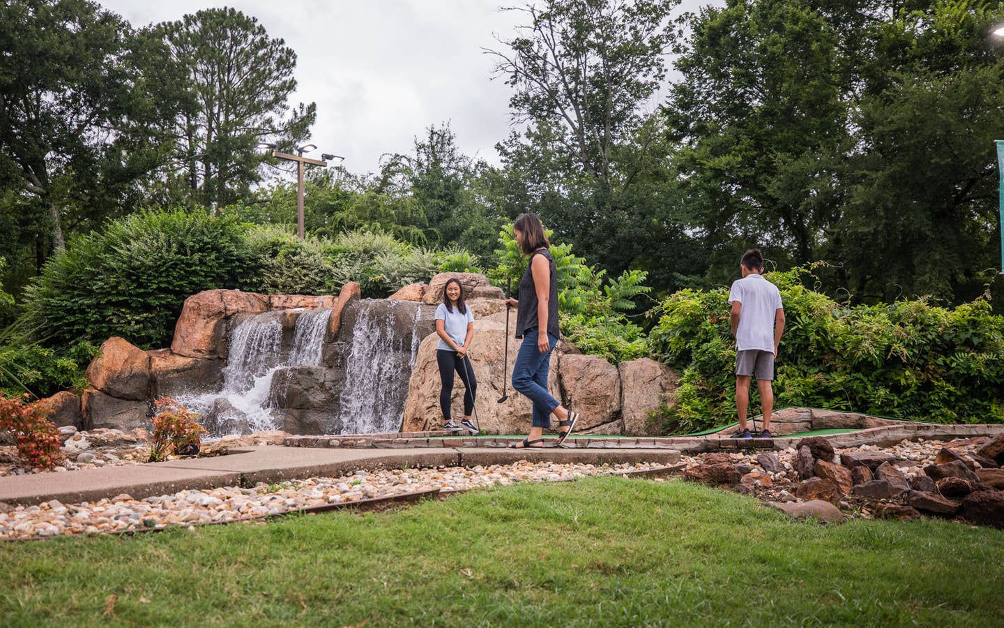 Three guests playing mini golf in front of waterfall at Villages Resort in Flint, Texas.