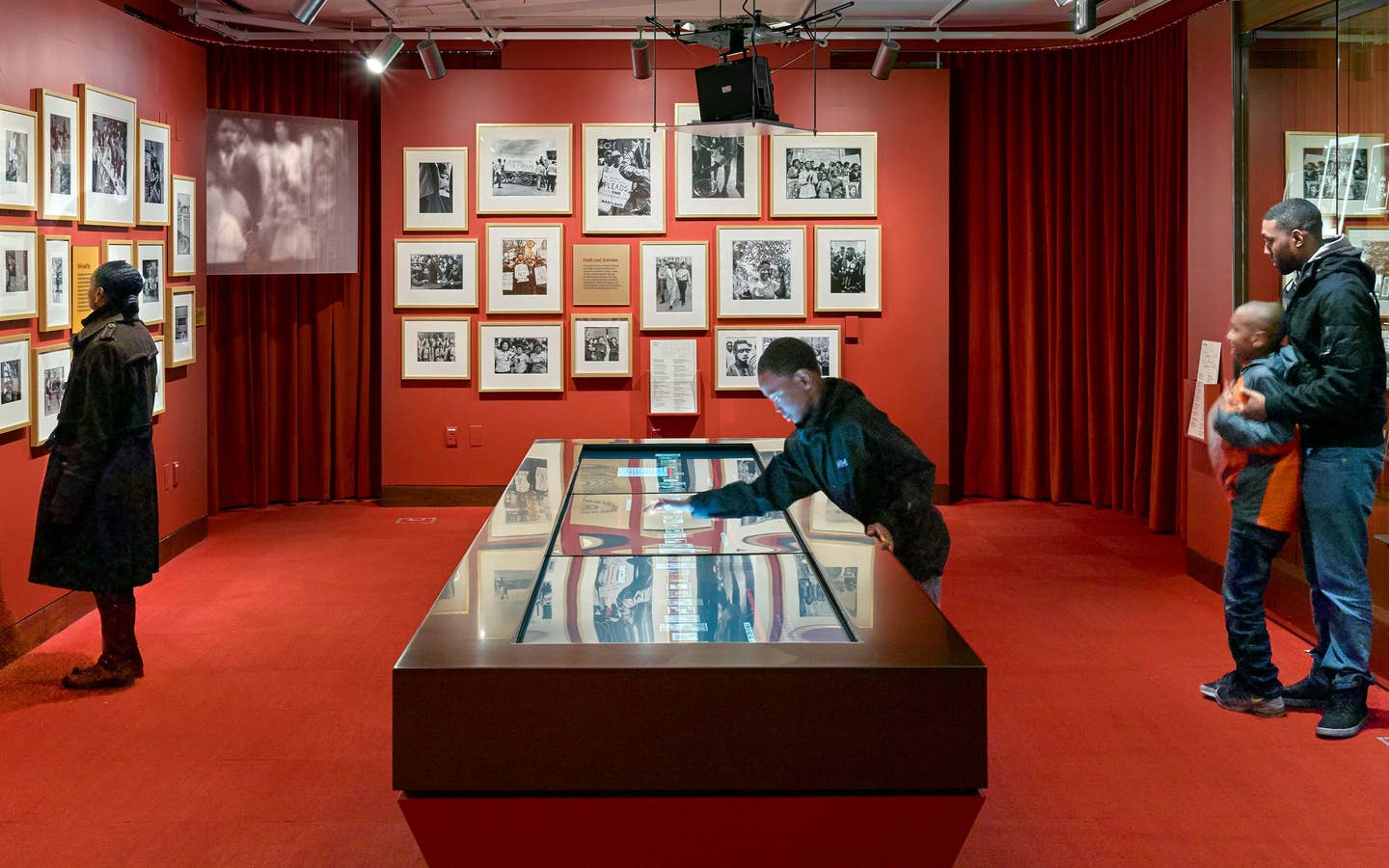 A woman, two young boys and a man stand in a red room curated with photography and video displays.