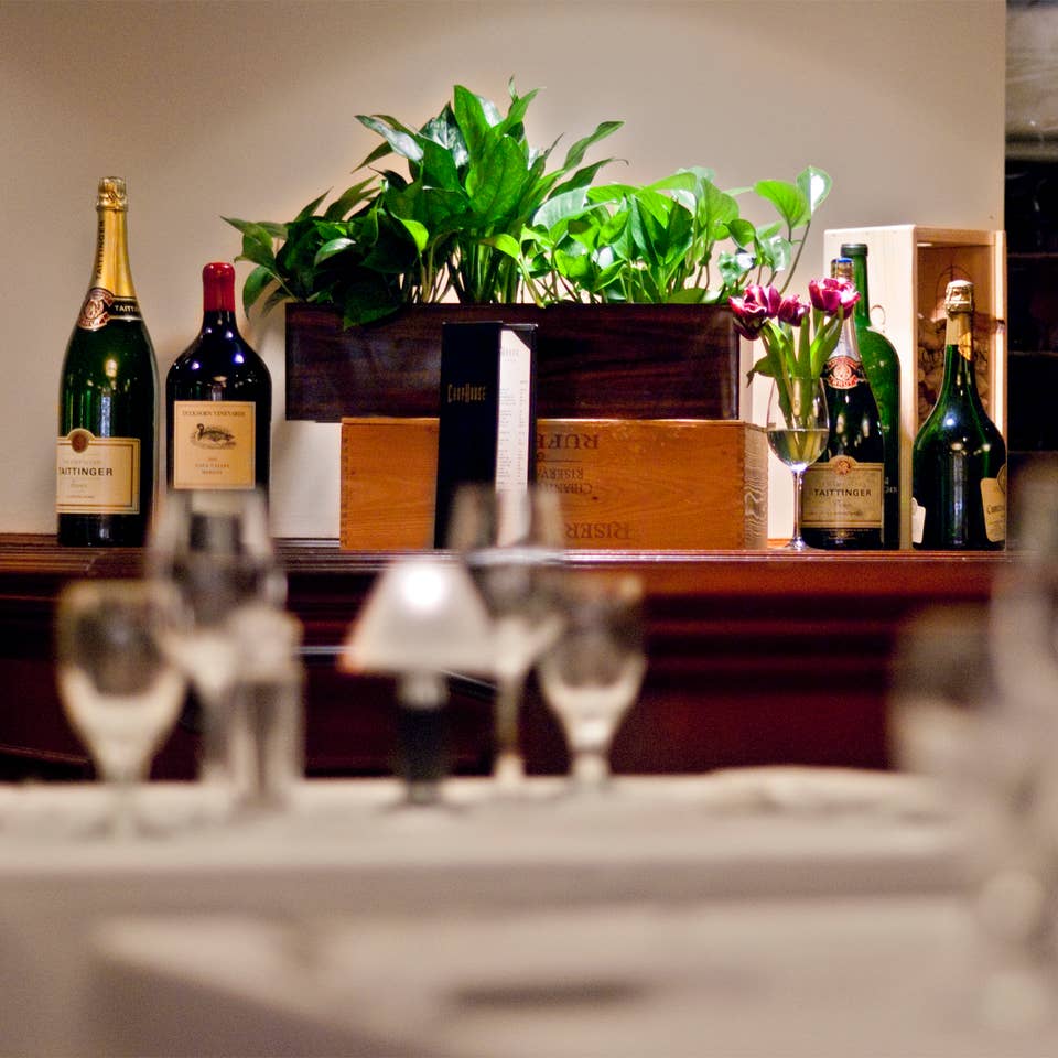 Restaurant table with wine glasses and bottles of wine in the background.