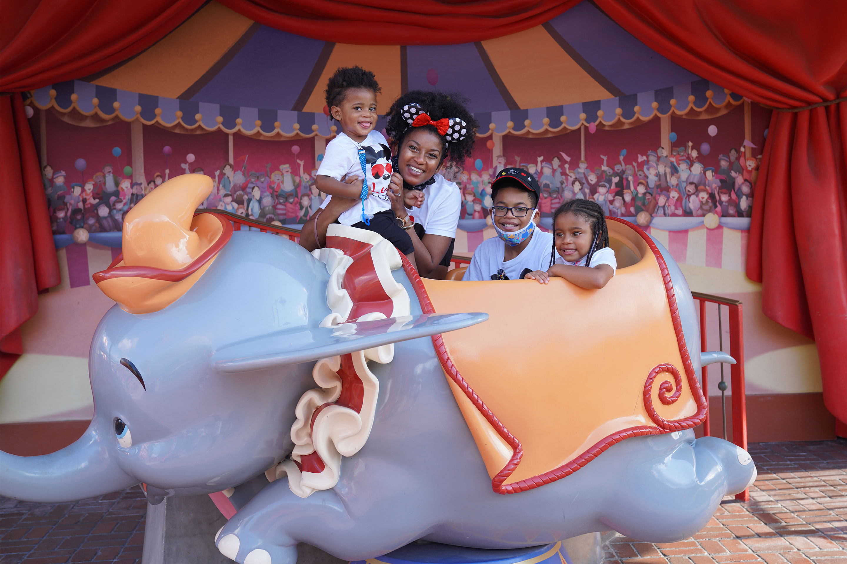 Featured Contributor, Tina Meeks, poses with her daughter and sons on a Dumbo ride vehicle located in Magic Kingdom at Walt Disney World resort.