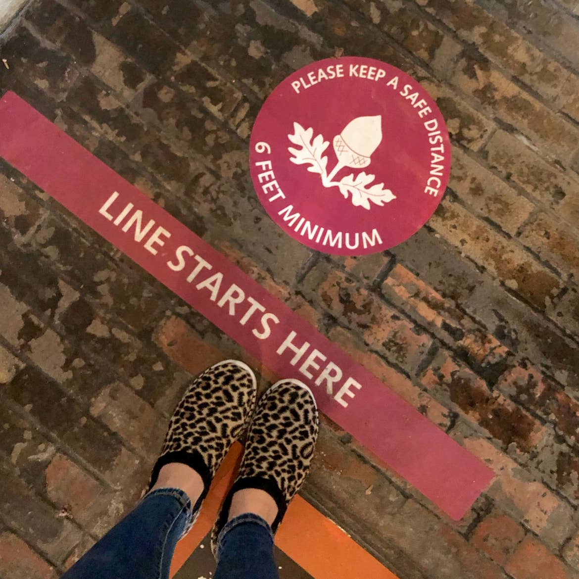 A brick-paved floor of the Biltmore Estate with a sign indicating Safety Measures for Social Distancing that reads, 'Line starts here, Please keep a safe distance, 6 Feet Minimum.'