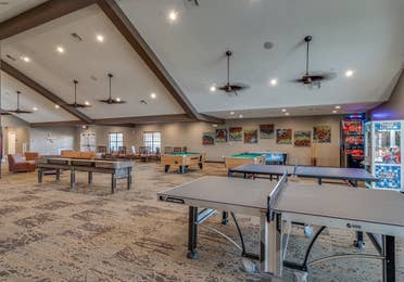 Game room with two ping pong tables, two pool tables, a pop-a-shot machine, claw machine, and seating at Piney Shores Resort in Conroe, Texas.