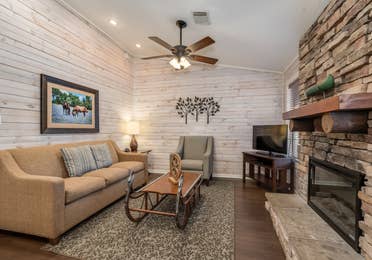 Living room with couch, accent chair, flat screen TV, and fireplace in a two bedroom cabin at Piney Shores Resort in Conroe, Texas