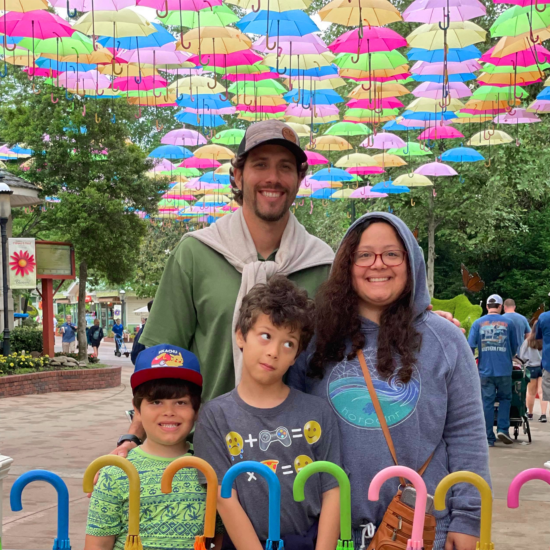 A family of four stand under a colorful umbrella display outdoors.