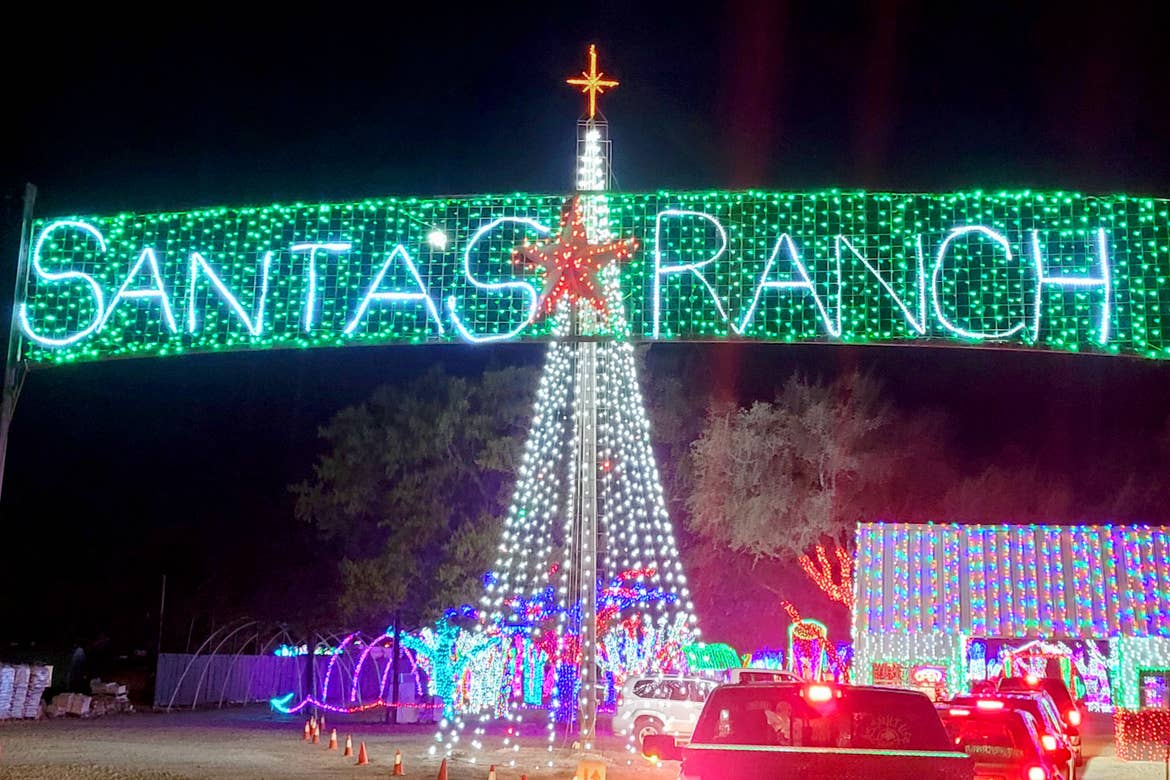 A string light sign that reads, 'Santa's Ranch' with a green background and red star stands in front of a white LED Christmas tree.