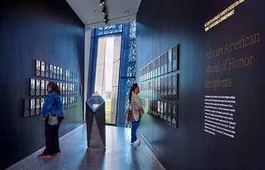 Two women stand in a black hallway curated with photography, statues and supportive signage.