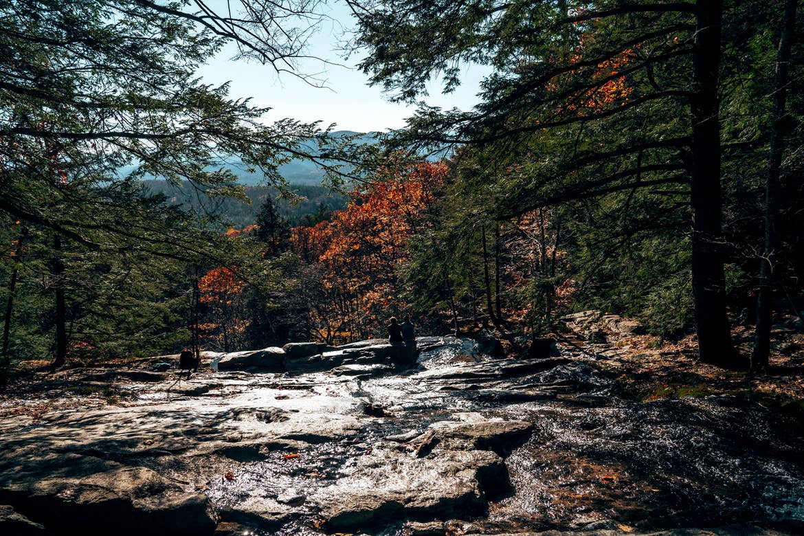 Fall foliage appears on trees overlooking a rock and waterfall formation.