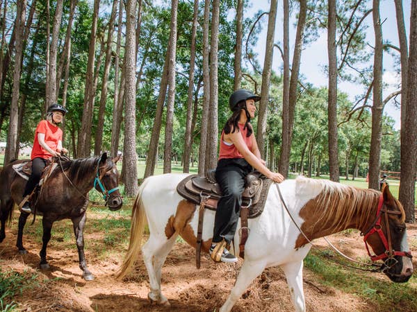 Two guests riding horses in forest at Villages Resort in Flint, Texas.