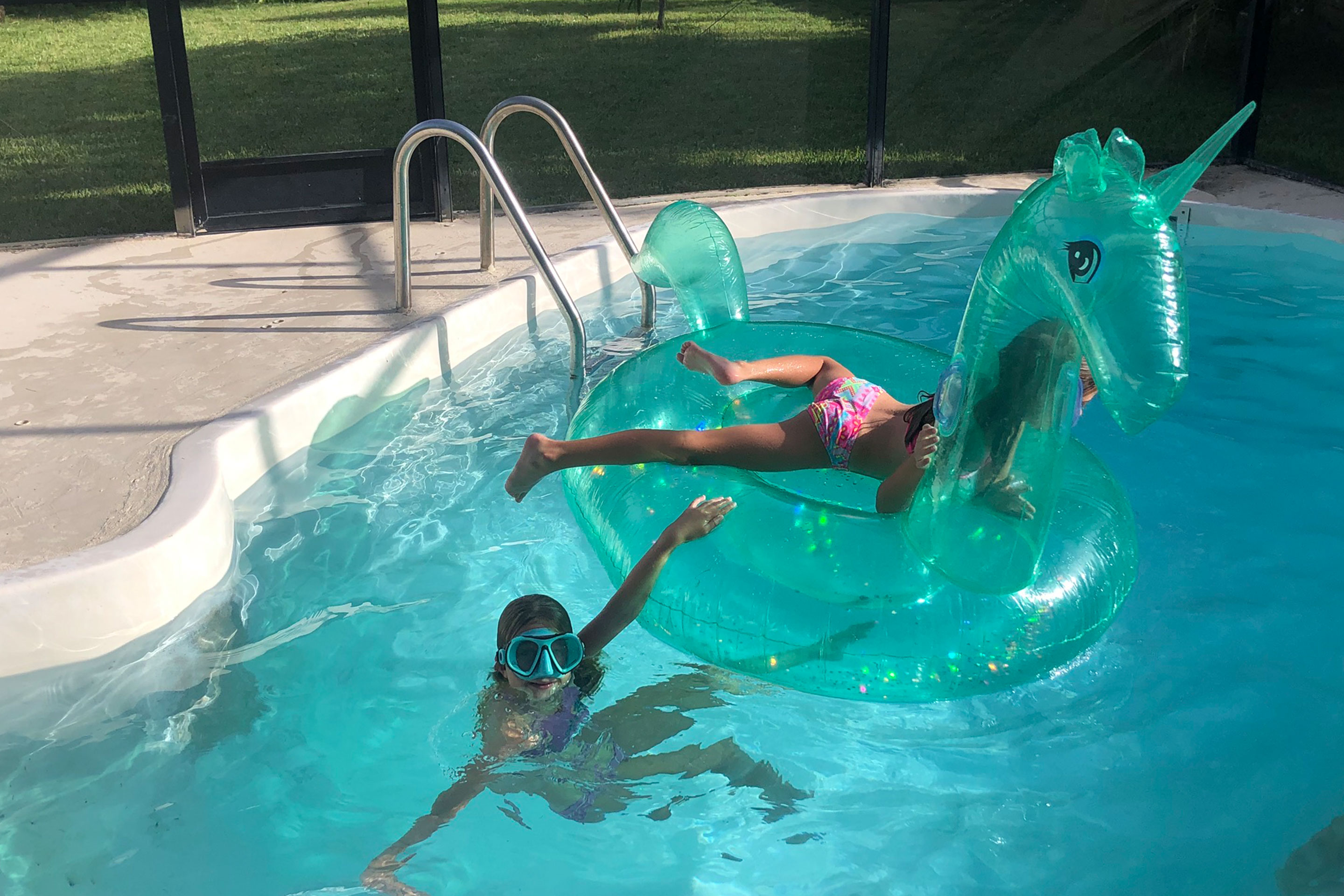 Featured Contributor, Chris Johnston's two daughters, Kyler (left) and Kyndall (right), wear snorkel gear while swimming in the pool around an inflatable unicorn tube.